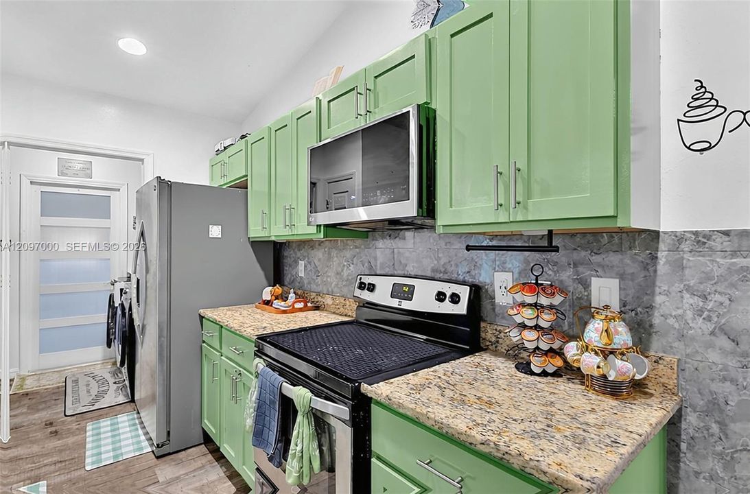 Kitchen featuring green cabinetry, speckled stone countertops, grey tile backsplash, built-in stainless steel microwave, and wood-finish flooring