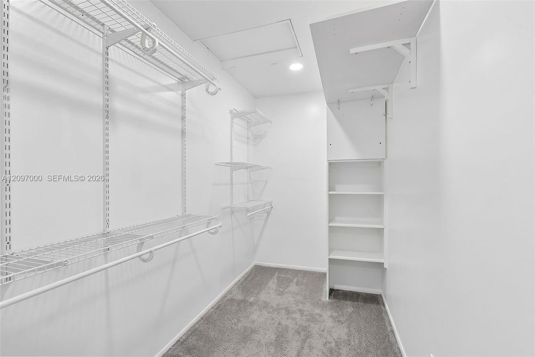 Walk-in closet featuring white wire shelving, wall-mounted white laminate organizer with fixed shelving, recessed lighting, and carpeting