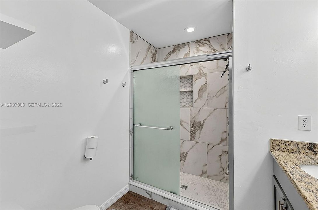Walk-in shower with floor-to-ceiling large format patterned tile, integrated recessed shelving, hexagonal mosaic tile shower floor, frosted glass sliding door, and stone countertop vanity