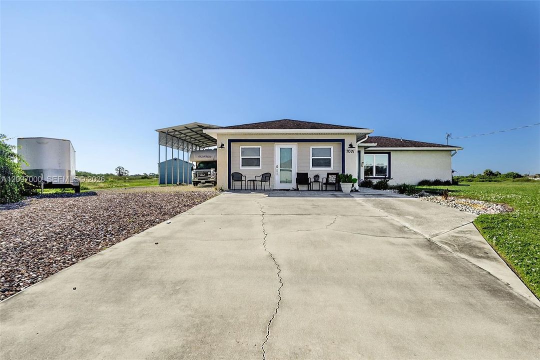 Exterior featuring a stucco facade, hipped roofline, concrete driveway, and a detached metal carport structure