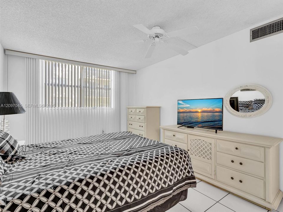 Room featuring white tile flooring, vertical window blinds, and a ceiling-mounted fan with integrated lighting
