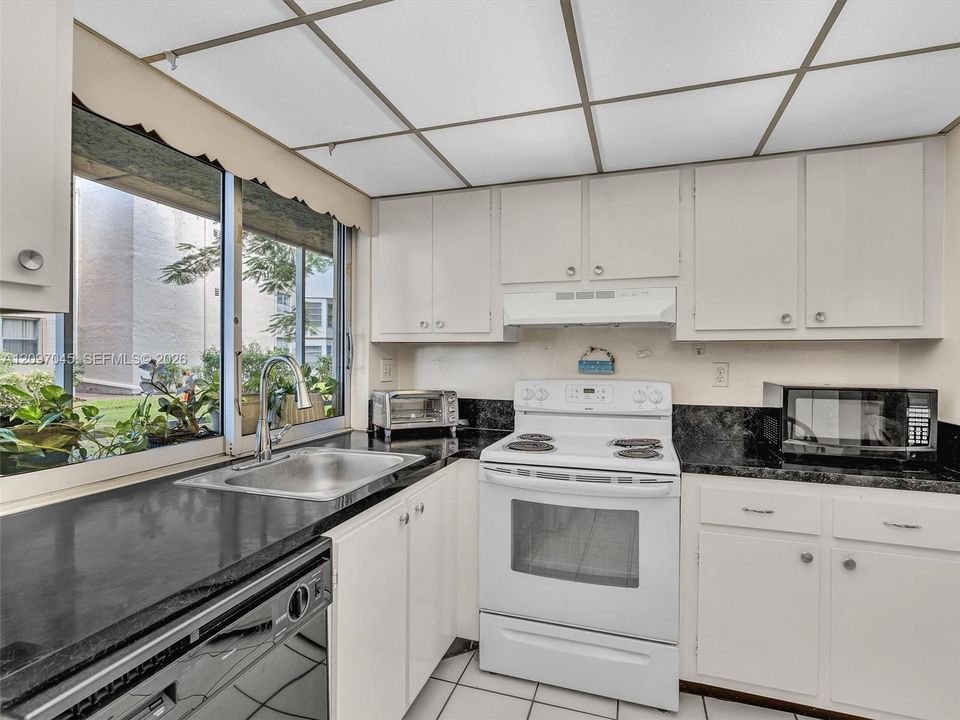 Kitchen featuring white shaker-style cabinetry, dark stone countertops, an integrated drop-in stainless steel sink, a white electric range, and ceramic tile flooring