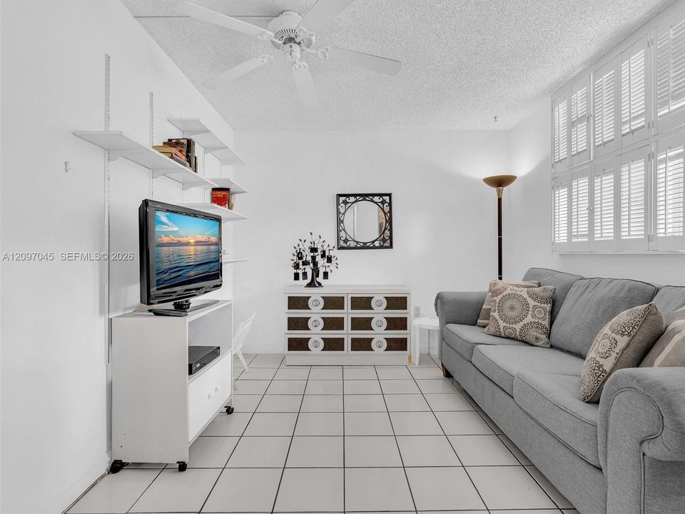 Light-filled room featuring white tile flooring, ceiling-mounted fan, and wall-mounted shutters