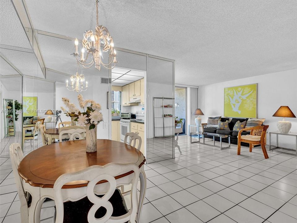 Open-concept interior featuring large-format ceramic tile flooring, floor-to-ceiling mirror paneling, and an ornate multi-arm chandelier