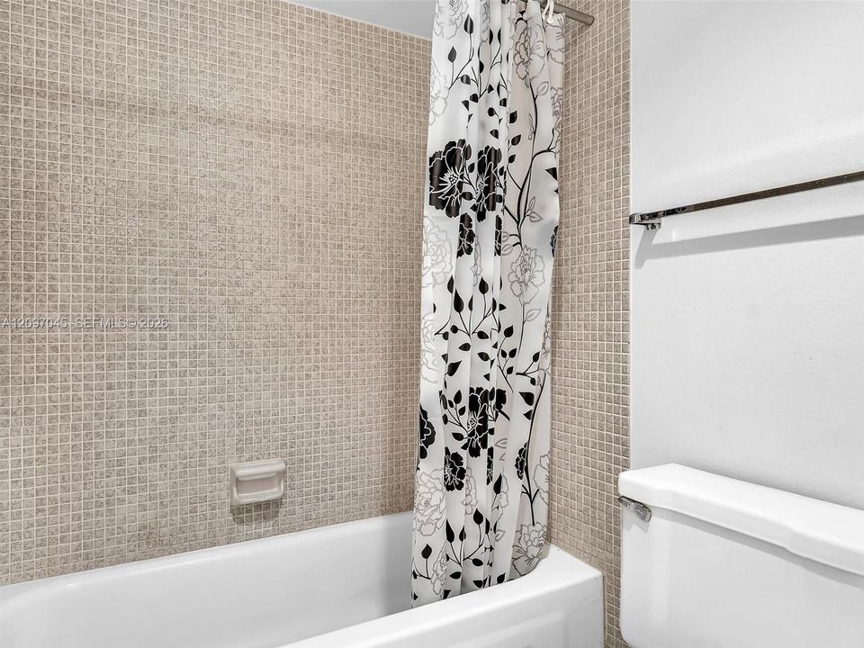Bathroom featuring a white bathtub, beige mosaic tile surround, built-in recessed soap dish, and a wall-mounted metal towel rack