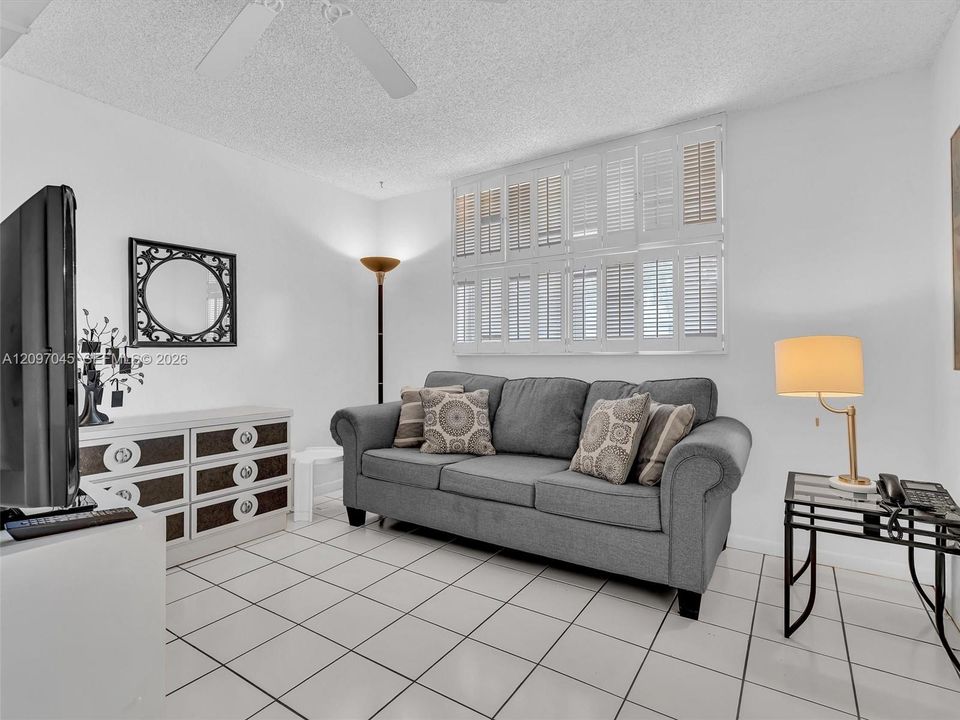 2nd bedroom featuring white ceramic tile flooring, plantation shutters,  ceiling fan and pull out couch-bed