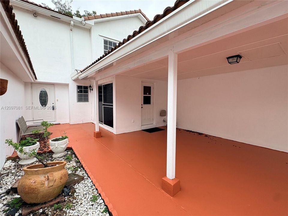 Covered patio featuring a solid-surface floor, two exterior entry doors, and a gravel-lined landscape bed