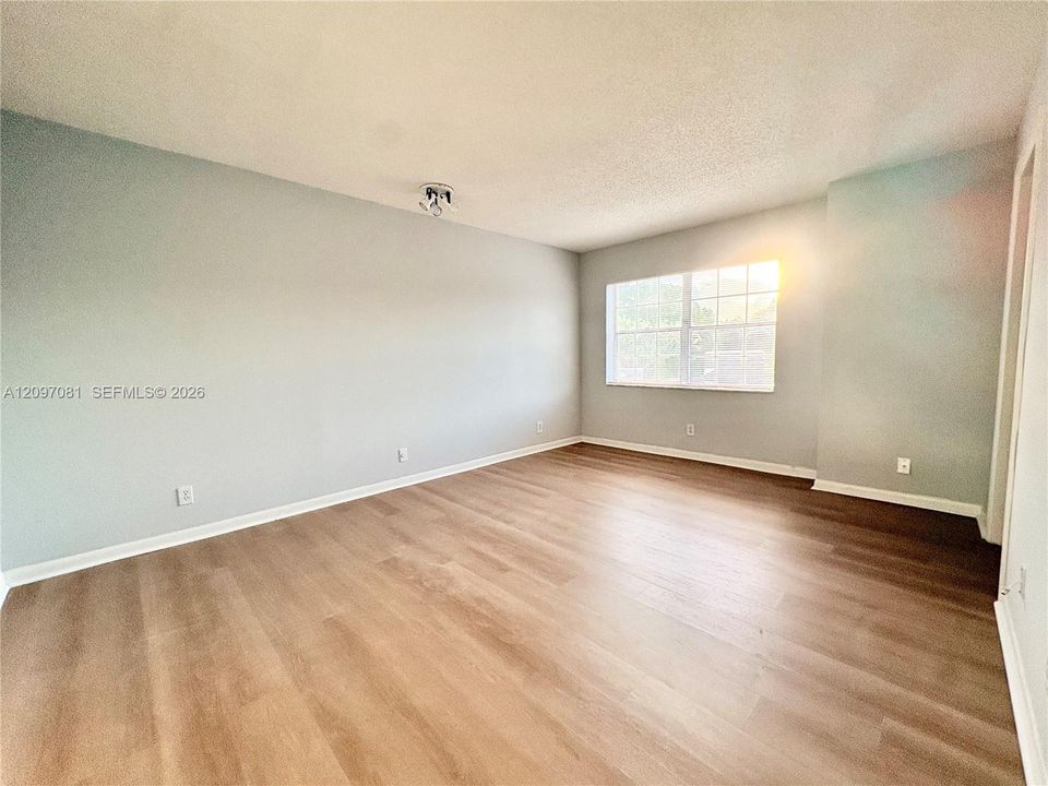 Neutral-toned interior space featuring wood-finish flooring, multi-pane window, and overhead ceiling-mounted lighting