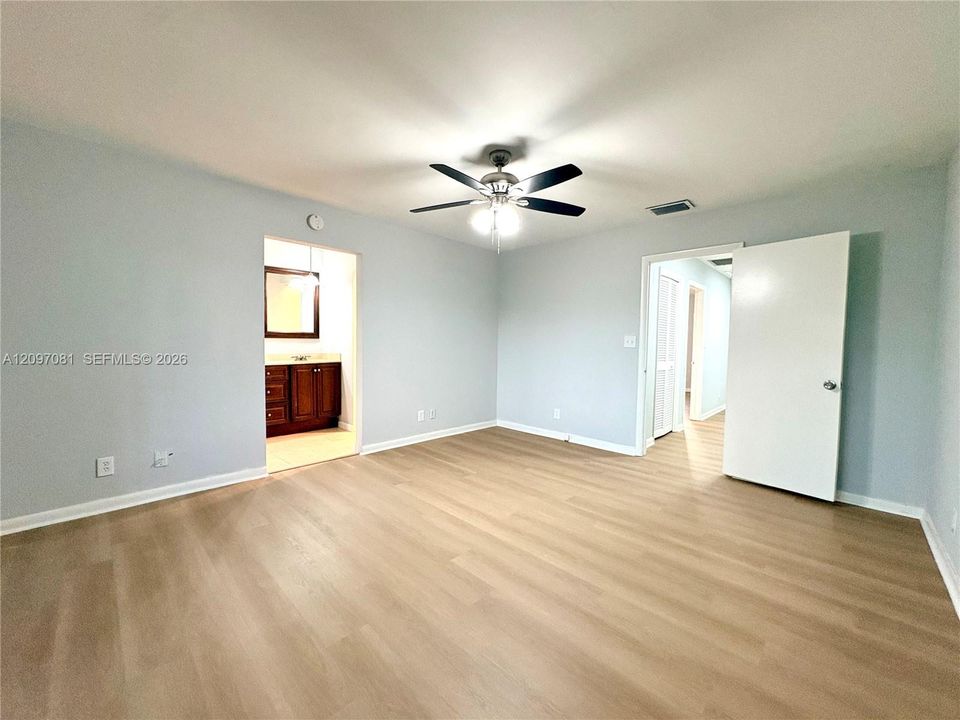 Neutral-toned interior featuring wood-finish flooring, a ceiling fan with integrated lighting, and solid-core doors