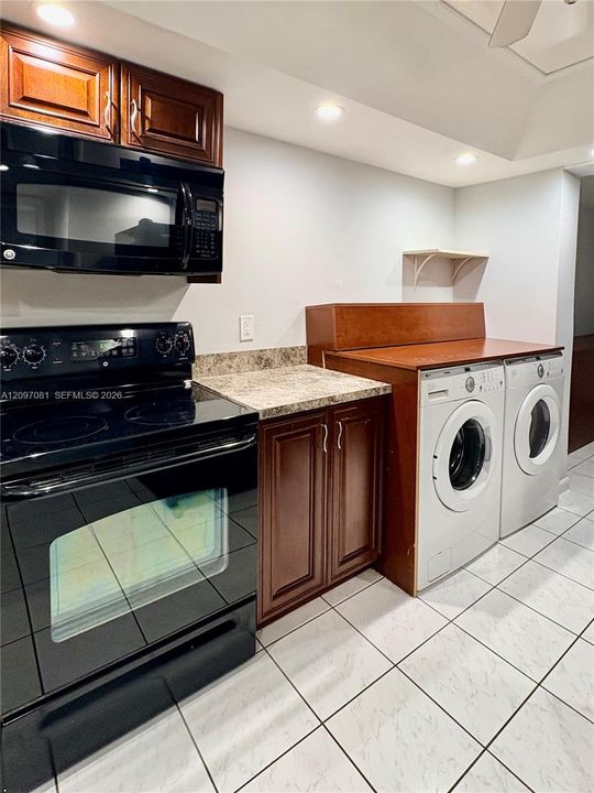 Custom cabinetry with rich wood finish, stone-patterned countertops, black electric range with over-the-range microwave, and ceramic tile flooring