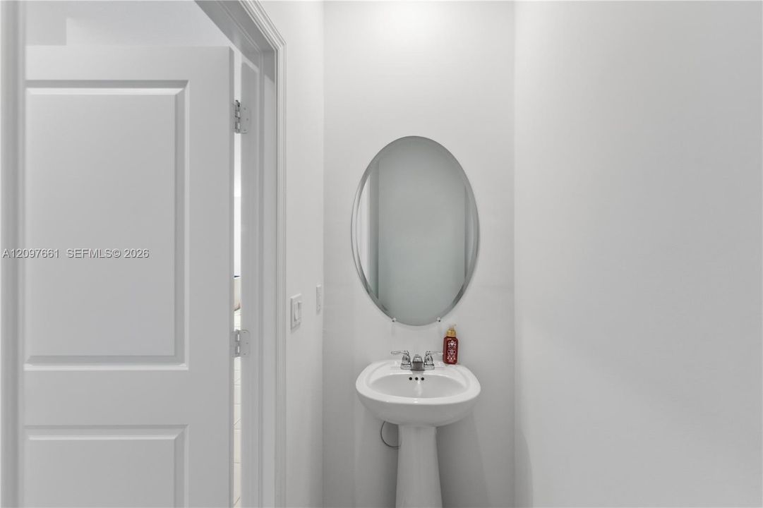 Oval wall-mounted mirror featuring a polished edge, complemented by a white pedestal sink with a chrome dual-handle faucet and a paneled interior door