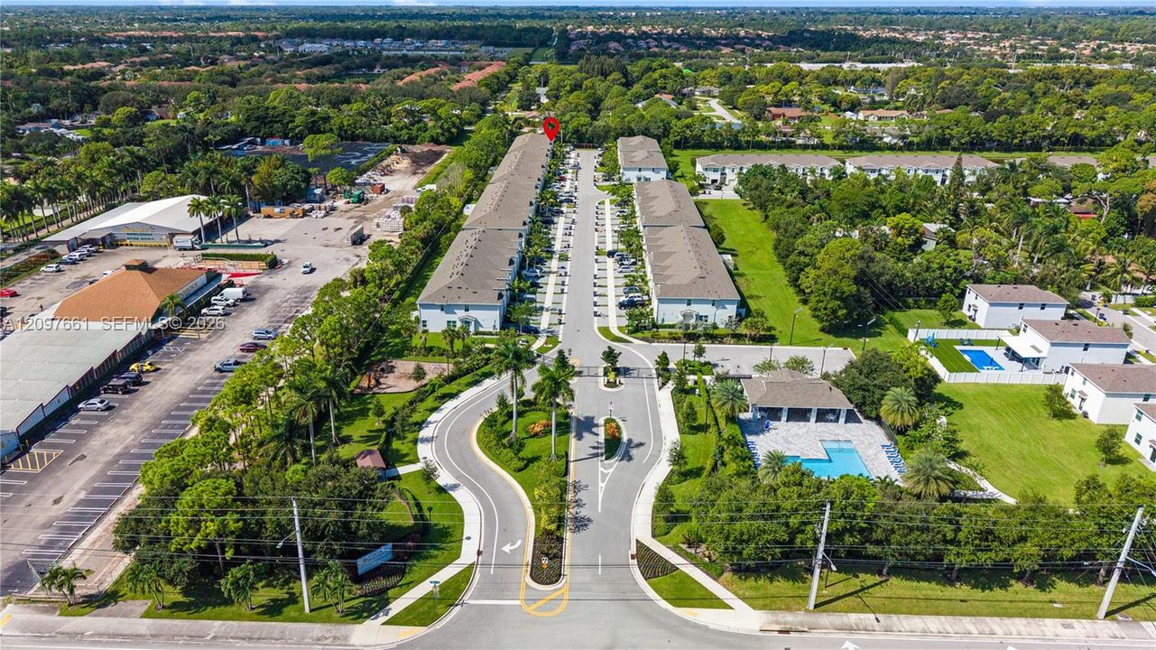 Aerial perspective of the residential complex featuring multi-unit structures with shingled roofing, paved private roadways, landscaped green space, and an outdoor swimming pool
