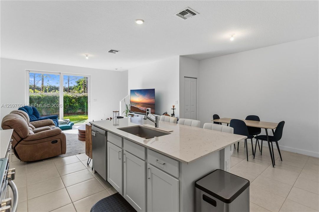 Kitchen island featuring a rectangular undermount sink, stone-composite countertop, and Shaker-style cabinetry, complemented by large-format tile flooring and sliding glass doors
