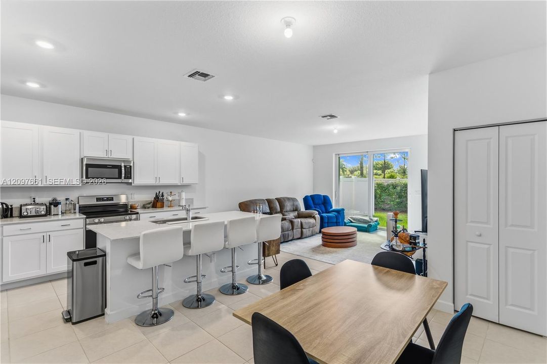 Kitchen featuring white cabinetry, solid-surface countertops, center island with bar seating, integrated stainless steel appliances, and tile flooring