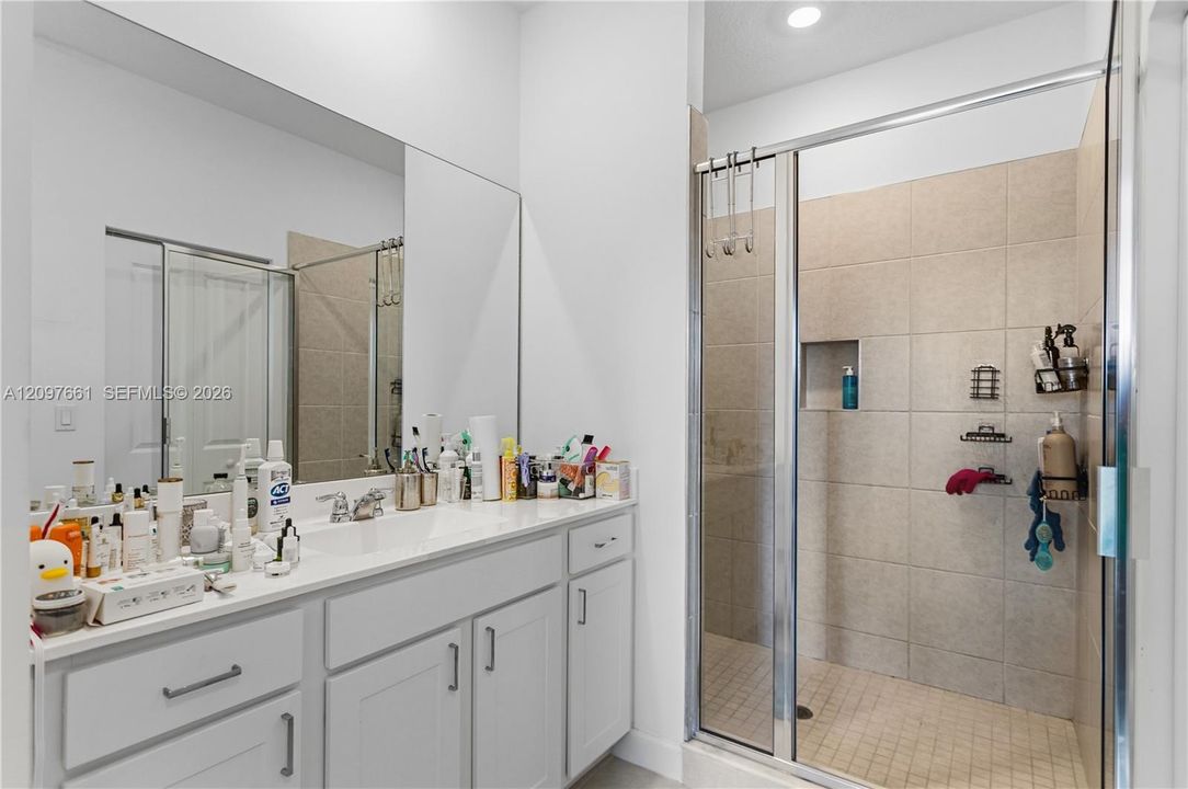 White vanity featuring a solid surface countertop with integrated basin, full-width mirror, walk-in shower with tile surround, and built-in recessed wall niche