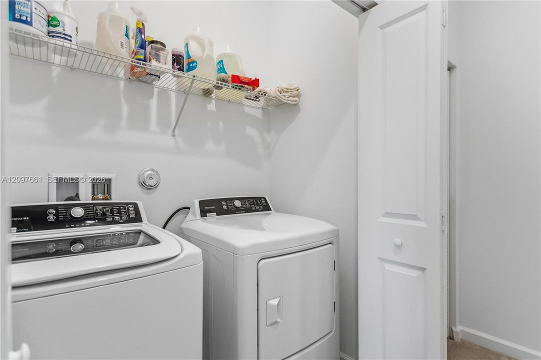Laundry area featuring white top-load washer and dryer, wall-mounted wire shelving, and a paneled closet door