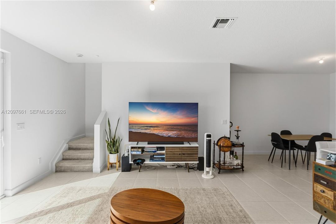 Open-concept interior featuring neutral-toned tile flooring, recessed ceiling lighting, and carpeted stairs with a partial wall partition
