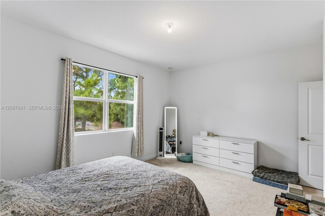 Neutral-toned carpeted flooring, white interior walls, and a large dual-pane window featuring exterior tree-lined scenery