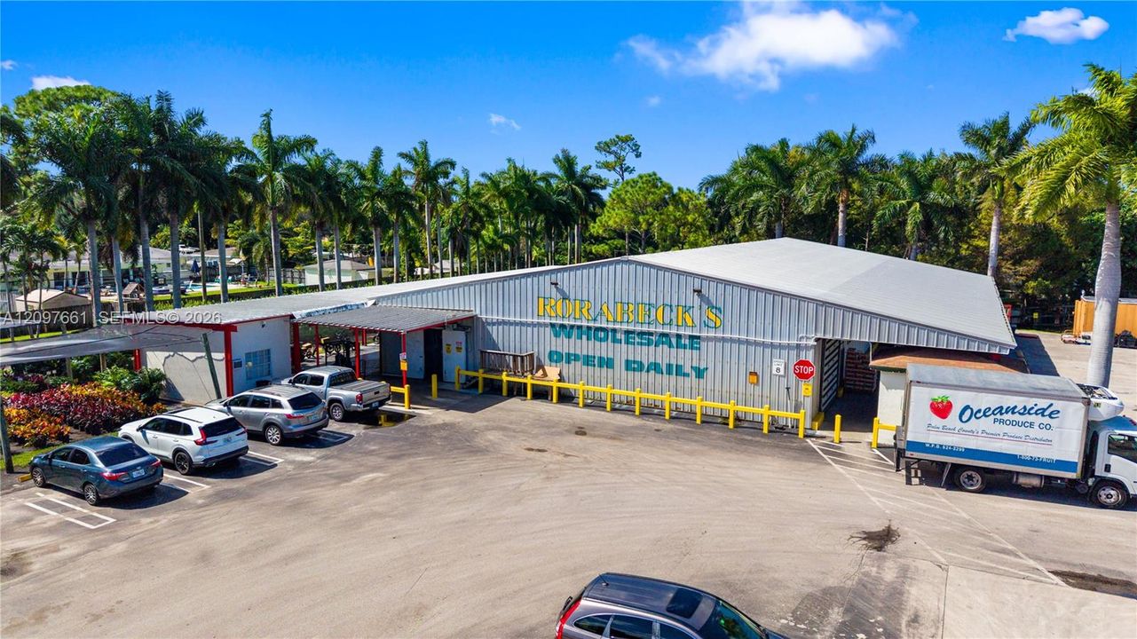 Industrial warehouse facility featuring metal siding, a wide-span gable roof, dedicated paved parking area, and mature perimeter landscaping