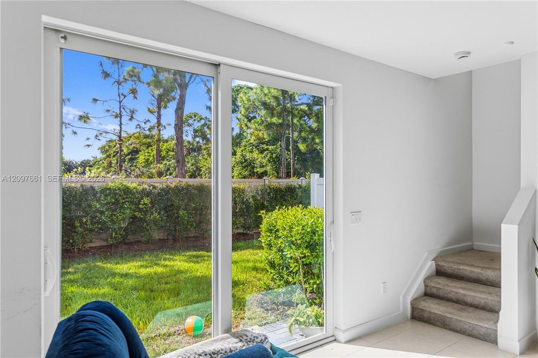 Large sliding glass doors with white frames, neutral tile flooring, and carpeted stairs with a solid partition