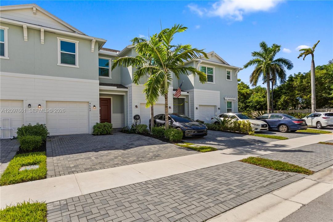 Two-story exterior featuring light-colored siding, paver driveways, attached garages, and mature palm landscaping