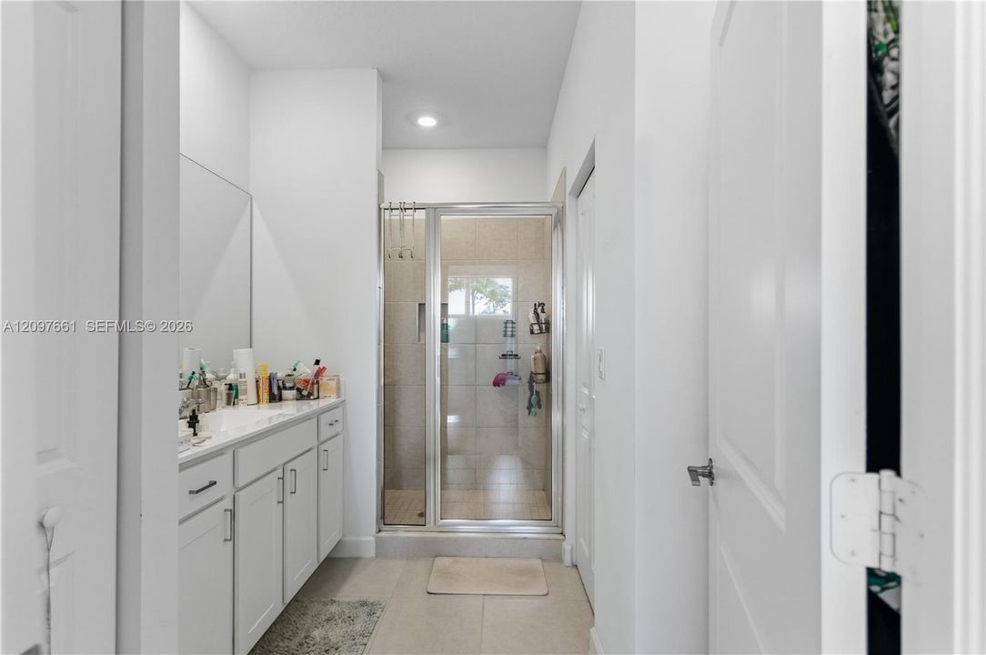Bathroom featuring a white vanity cabinet with an integrated sink, a large wall-mounted mirror, recessed lighting, and a glass-enclosed shower with tiled interior
