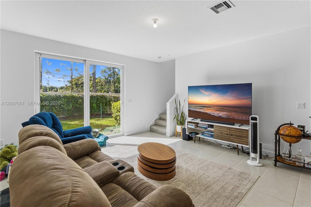 Living area featuring large-format tile flooring, sliding glass doors, and a staircase with carpeted treads