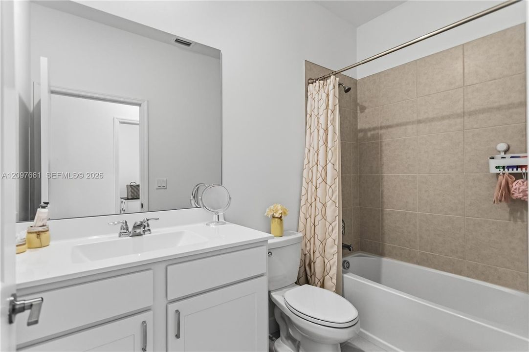 White vanity with solid surface countertop and integrated rectangular sink, large wall-mounted mirror, and tiled shower-tub combination