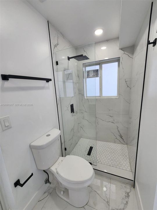 Bathroom featuring large-format tile flooring, a glass-enclosed shower with hexagon floor tile, matte black hardware, and an integrated shower head