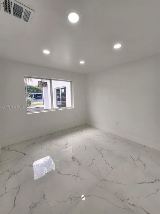 Large-format, light-toned flooring with decorative veining, recessed ceiling lighting, and a single-pane horizontal window