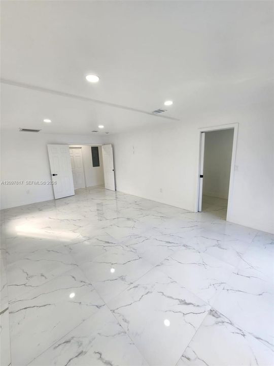 Interior space featuring white-toned stone-finish flooring, recessed lighting, and white paneled doors with matte black hardware