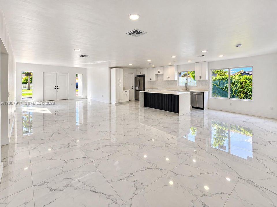 Open-concept interior featuring large-format tile flooring, recessed lighting, white cabinetry, and a kitchen island with a contrasting dark base and white countertop