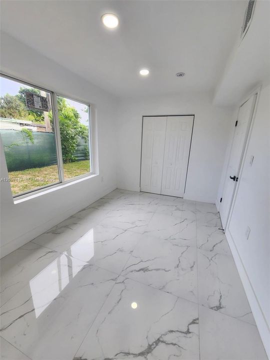 Large-format stone-look tile flooring with veining detail, recessed lighting, and a dual-panel closet door