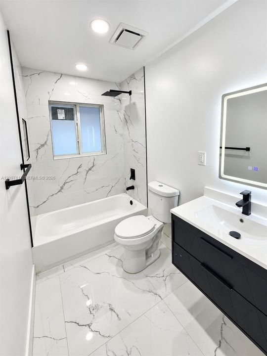Bathroom featuring large-format stone-patterned tile flooring and wall surrounds, dark finish floating vanity with white countertop, matte black fixtures, and a wall-mounted LED mirror