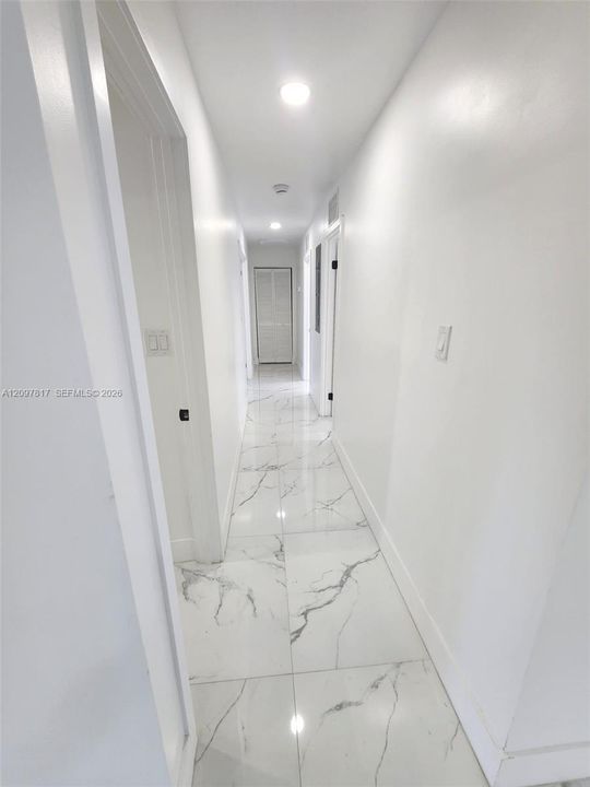 Hallway featuring large-format tile flooring with veined detailing, recessed ceiling lighting, and crisp white wall finishes