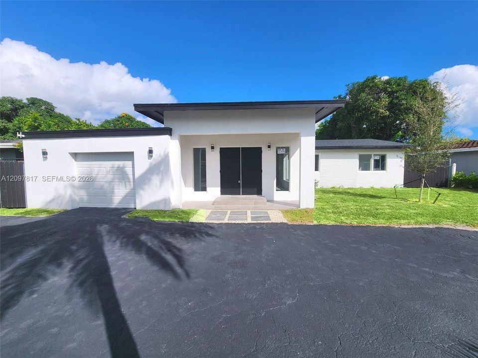 Contemporary single-story exterior featuring a flat roofline, white smooth-finish facade, double-door entryway, attached garage, and a paved driveway
