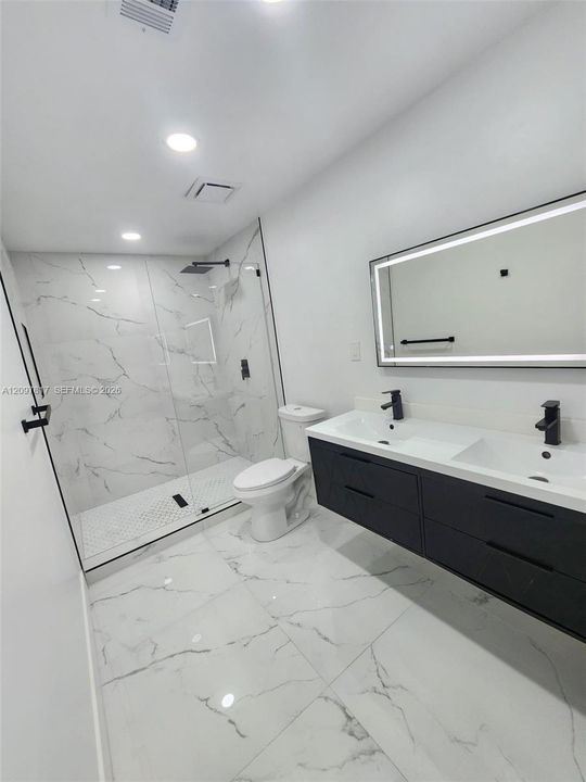 Floating double vanity with matte black faucets, oversized walk-in shower with glass enclosure, wall-to-wall stone-finish tile flooring, and integrated LED-backlit mirror