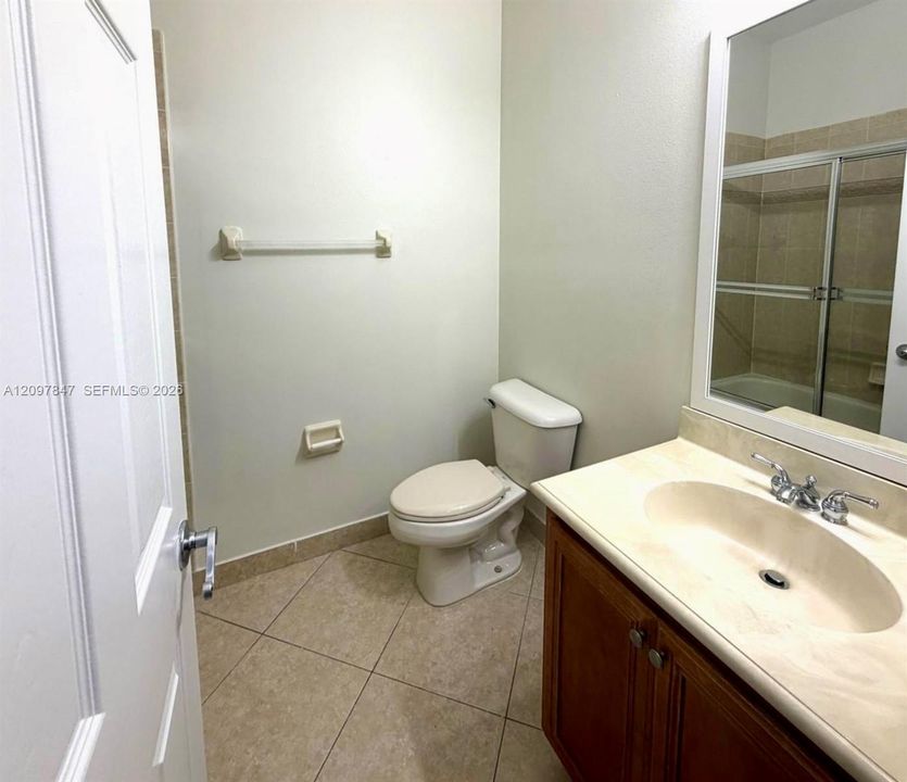 Bathroom featuring a wood-finish vanity with an integrated sink, neutral stone-finish tile flooring, a wall-mounted mirror, and a shower enclosure with sliding glass doors