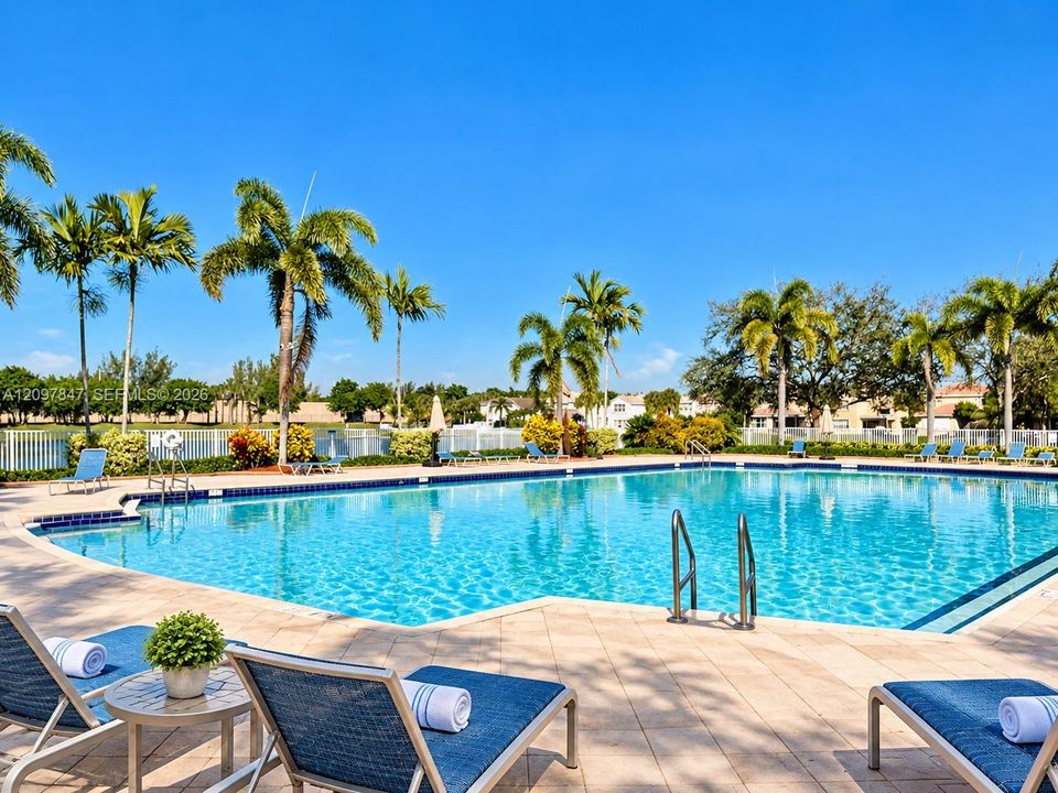 Swimming pool with a paved deck, metal ladder entries, perimeter fencing, and surrounding palm trees
