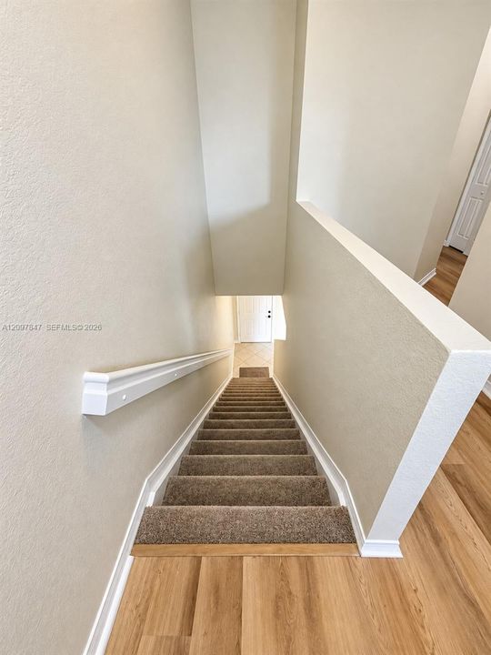 Staircase featuring wall-to-wall carpeting, a white-painted wooden handrail, neutral-toned wall paint, and wood-finish flooring at the landing