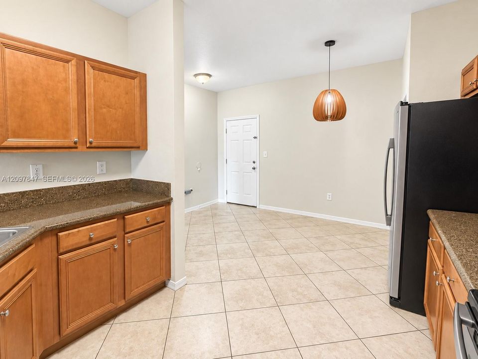 Kitchen featuring medium-tone wood cabinetry, solid-surface countertops, tile flooring, and a decorative pendant light fixture