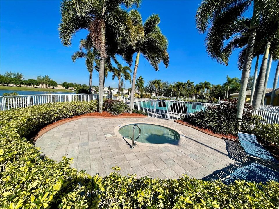 In-ground spa with a paver deck, white perimeter fencing, and mature palm landscaping overlooking the water