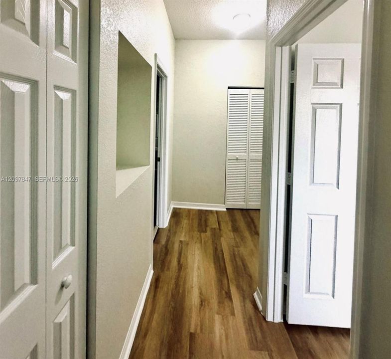 Hallway featuring wood-finish flooring, two sets of white paneled closet doors, one louvered closet door, and a built-in wall niche