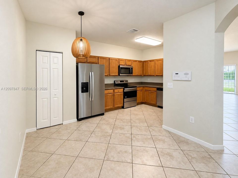 Kitchen featuring wood cabinetry, stainless steel appliances, ceramic tile flooring, and a spherical pendant light fixture