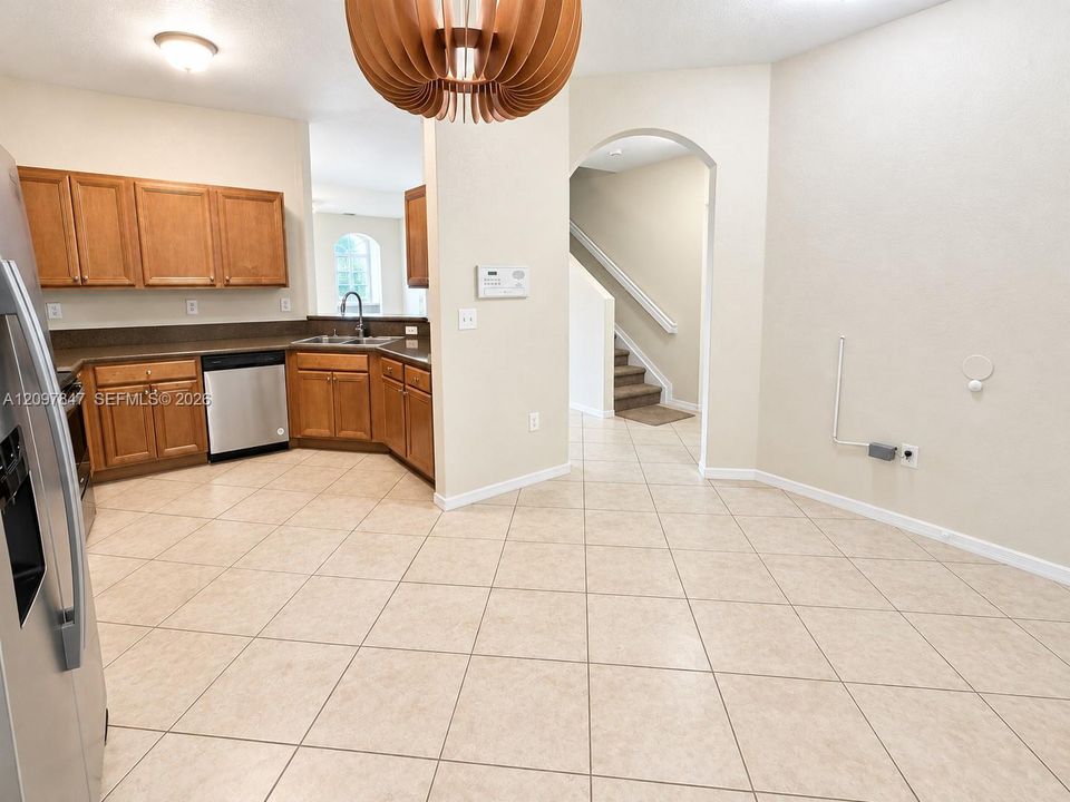 Kitchen featuring wood cabinetry, stainless steel appliances, tile flooring, and an architectural pendant light fixture, incorporating a rounded archway