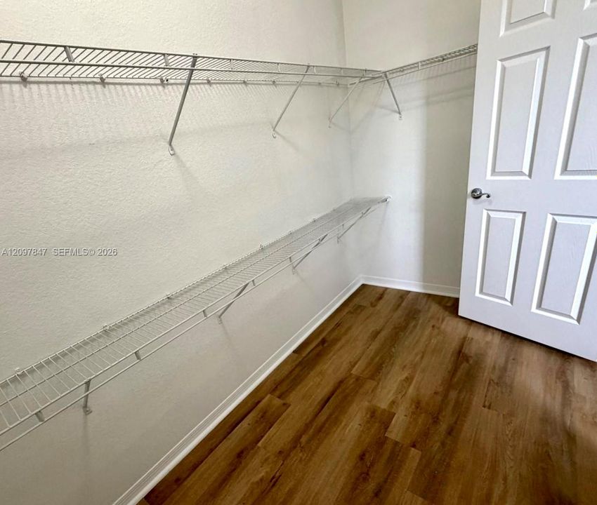 Storage area featuring wood-finish flooring, white-painted walls, a multi-panel door with a metallic knob, and wall-mounted wire shelving