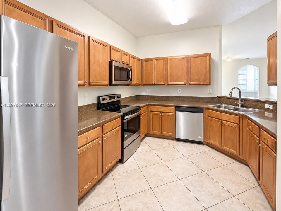 Kitchen featuring shaker-style wood cabinetry, stone-surface countertops, stainless steel appliances, a double-basin undermount sink, and tiled flooring