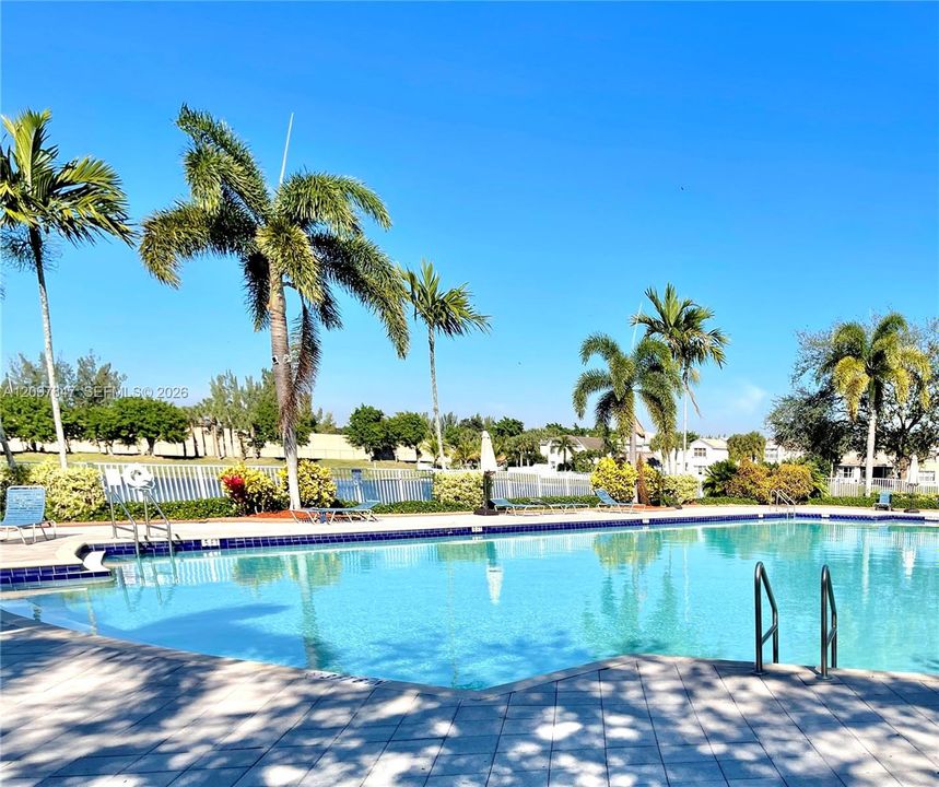 Swimming pool with blue tile border, paver stone deck, metal pool ladders, and mature palm tree landscaping