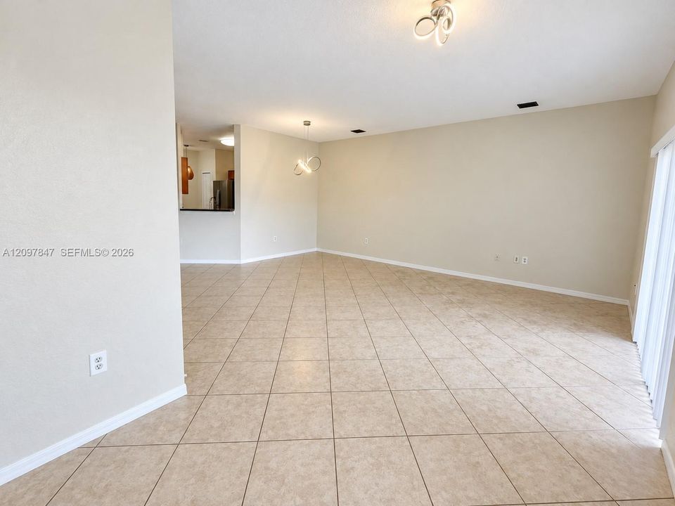 Spacious interior featuring neutral wall tones, ceramic tile flooring, modern sculptural ceiling light fixtures, and sliding glass doors