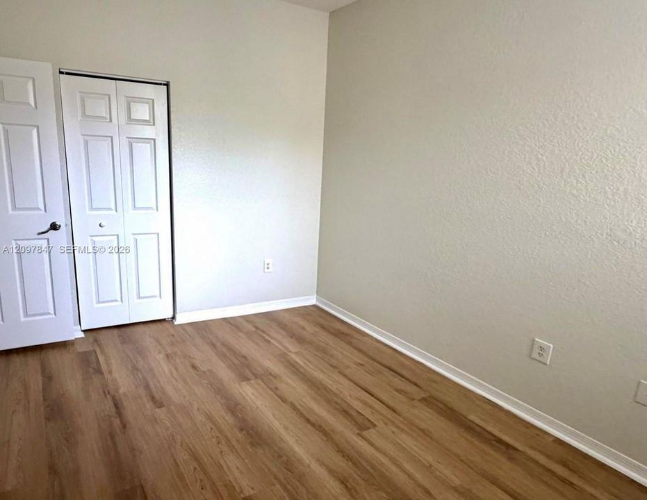 Room featuring neutral-toned walls, wood-finish flooring, and a white paneled closet door
